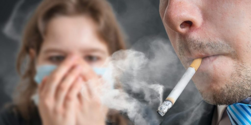Passive Smoking. Man Is Smoking Cigarette And Woman Is Covering Her Face. A Lot Of Smoke Around.