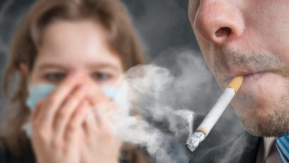 Passive Smoking. Man Is Smoking Cigarette And Woman Is Covering Her Face. A Lot Of Smoke Around.